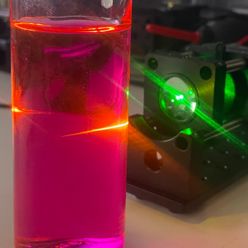 Laser shining into glass filled with fluorescent rhodamine b solution
